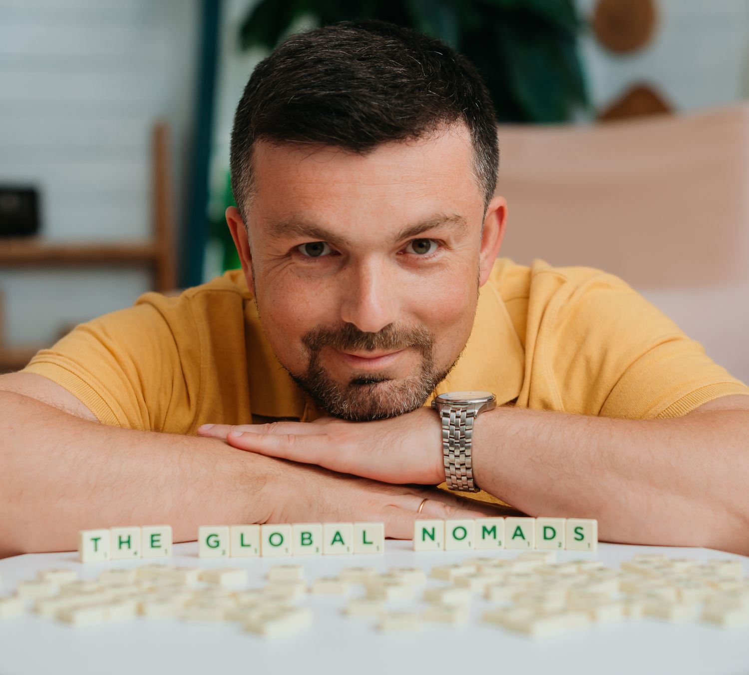 Sam Musayev, host of The Global Nomads' Podcast, smiling behind Scrabble tiles spelling The Global Nomads