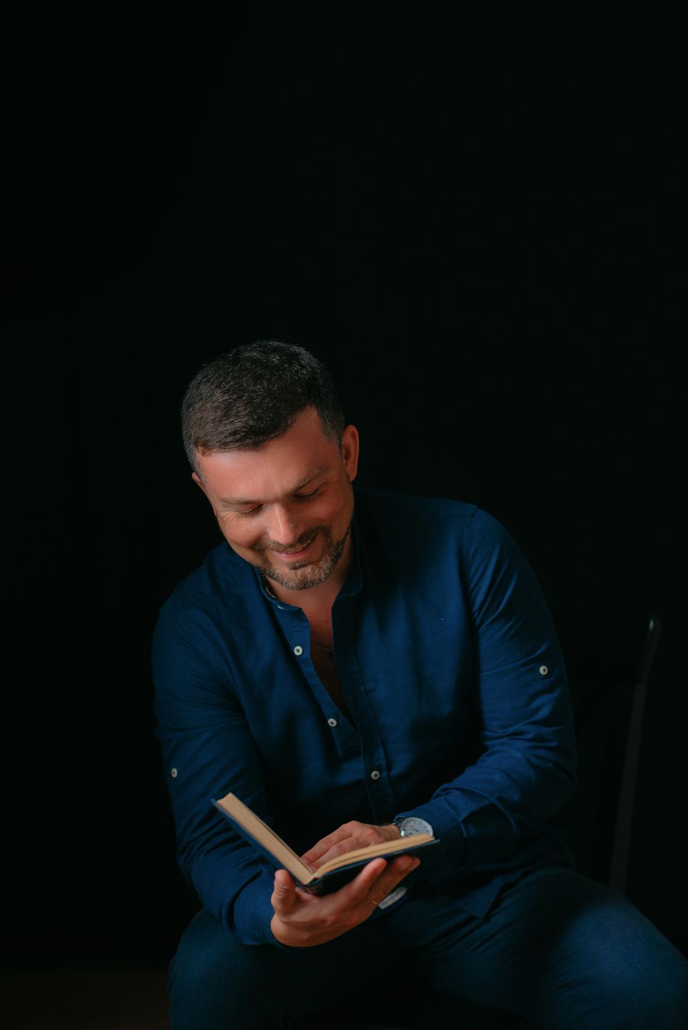 Sam Musayev reading a book, photographed against a black background